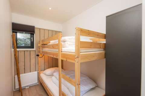 Schlafzimmer mit Etagenbett, Holzschrank und Fenster im Comfort Chalet, Veluwepark de Bosgraaf, Niederlande.