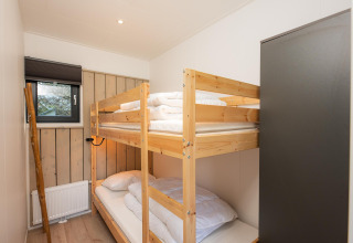 Schlafzimmer mit Etagenbett, Holzschrank und Fenster im Comfort Chalet, Veluwepark de Bosgraaf, Niederlande.
