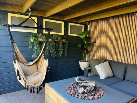 Gemütlicher Loungebereich im Veluwe Chalet mit Hängesessel, Feuerstelle und Pflanzen im Veluwepark de Bosgraaf.