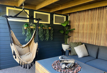 Coin salon chaleureux au Veluwe Chalet avec hamac, foyer, plantes et canapé à Veluwepark de Bosgraaf, Pays-Bas.