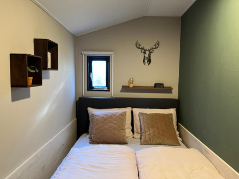Et hyggeligt soveværelse på Veluwe Chalet, Veluwepark de Bosgraaf, med dobbeltseng og hjortedekoration.