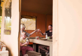 Familia comiendo y brindando dentro de una tienda safari en Wilsumer Berge, Alemania, vista interior cálida.