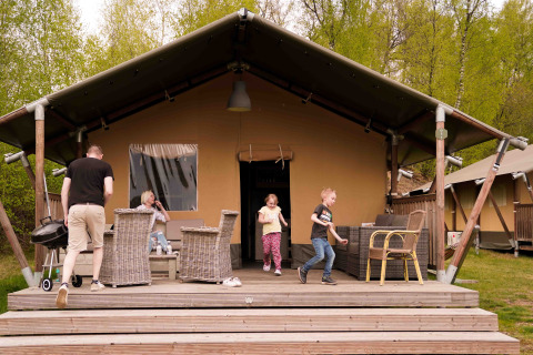 En familie hygger sig foran et safaritelt på Wilsumer Berge i Tyskland, omgivet af grønt område.