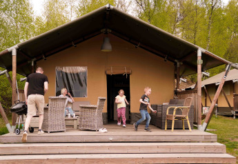 Familie entspannt vor einem Safarizelt im Wilsumer Berge, Deutschland, umgeben von grüner Natur.