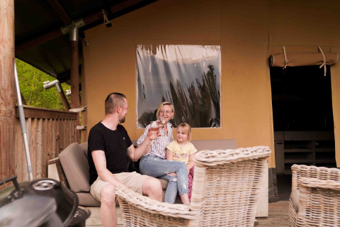 Familia relajándose frente a una tienda safari en Wilsumer Berge, Alemania, en una tarde soleada.