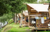 Tiendas safari en Petite Suisse, Bélgica, con terrazas de madera y ropa colgada en un entorno natural.