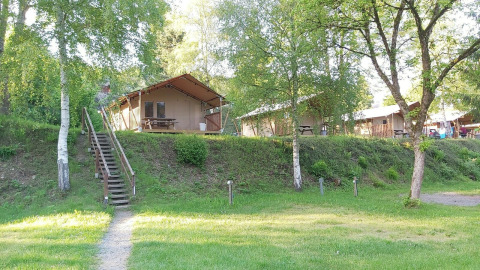 Safari-telt på Petite Suisse i Belgien med træer, grøn græsplæne og udendørs siddepladser om sommeren.