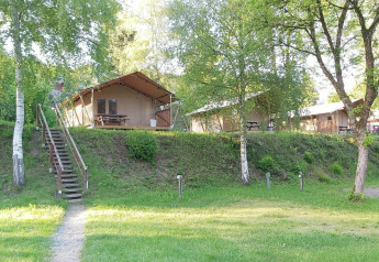 Safaritent bij Petite Suisse in België met houten trap, grasveld, bomen en picknicktafels buiten.