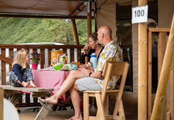 En familie nyder morgenmad ved et bord foran deres safaritelt på Petite Suisse campingplads i Belgien.