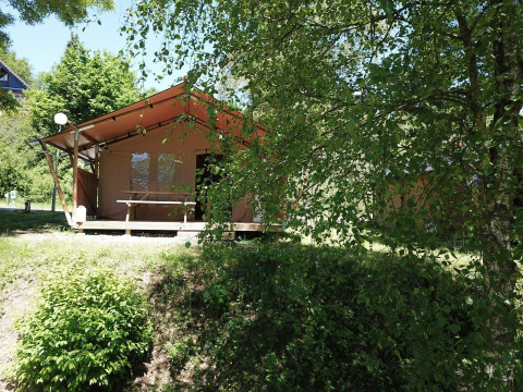 Tenda safari a Petite Suisse in Belgio, circondata da alberi e cespugli verdi in una giornata soleggiata.