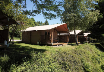 Tenda safari presso Petite Suisse in Belgio, circondata da alberi e natura sotto un cielo azzurro chiaro.