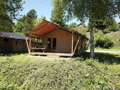 Safari-Zelt bei Petite Suisse in Belgien mit Holzrahmen und Veranda, umgeben von grüner Natur und Bäumen.