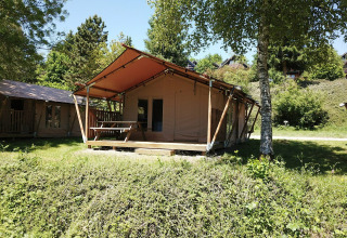 Safari-Zelt bei Petite Suisse in Belgien mit Holzrahmen und Veranda, umgeben von grüner Natur und Bäumen.
