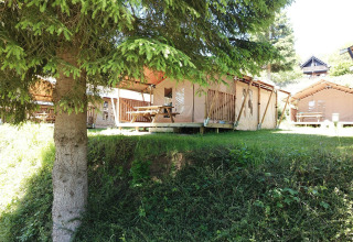 Safari-Zelte bei Petite Suisse in Belgien, umgeben von Bäumen, mit Picknicktisch im Sonnenschein.