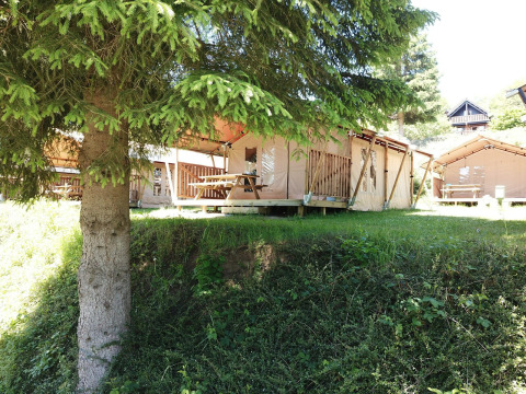 Safari tents at Petite Suisse in Belgium, surrounded by trees, with picnic tables on a sunny day.