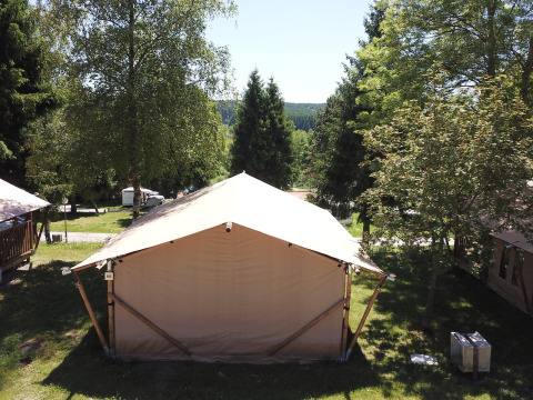 Safari-Zelt in Petite Suisse, Belgien, umgeben von Bäumen und grüner Natur bei Tageslicht.