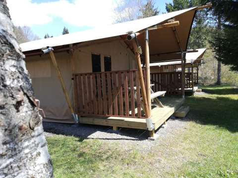 Tienda safari en Petite Suisse, Bélgica, con porche de madera y entorno natural verde, ideal para acampar.