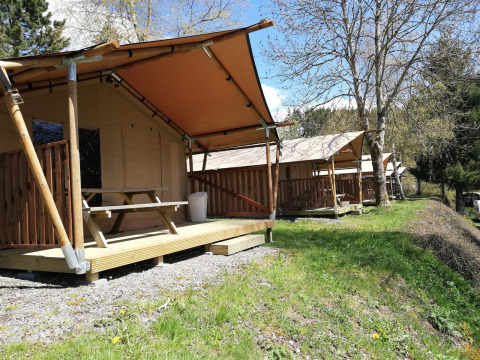Safari-telte ved Petite Suisse i Belgien, med træverandaer og picnicborde omgivet af natur.