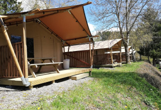 Tende safari a Petite Suisse in Belgio, con verande in legno e tavoli da picnic immersi nella natura.