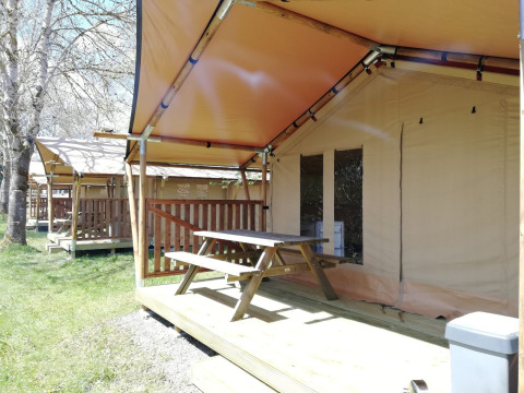 Tienda safari en Petite Suisse, Bélgica, con terraza de madera y mesa de picnic en un entorno natural y soleado.