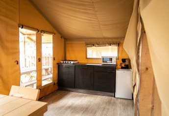 Interior view of the Safari tent at Petite Suisse in Belgium, featuring a kitchenette and wood table.