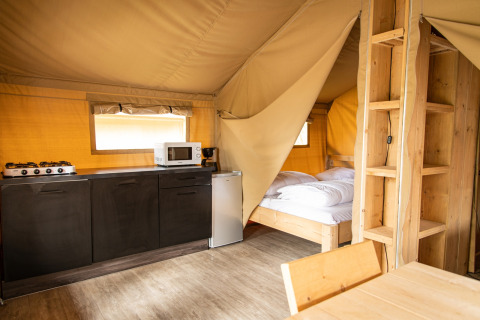Tienda safari en Petite Suisse, Bélgica, equipada con cocina, cama y muebles de madera, ambiente acogedor.