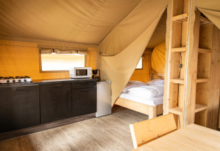 Tenda safari a Petite Suisse, Belgio, con cucina, letto e arredi in legno, atmosfera accogliente e moderna.