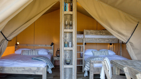 Interior de una tienda safari en Petite Suisse, Bélgica, con camas de madera y decoración acogedora.