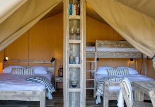 Interior de una tienda safari en Petite Suisse, Bélgica, con camas de madera y decoración acogedora.