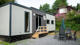 Un moderno lodge Taos XL en Petite Suisse, Bélgica, con mesa y sillas exteriores en un entorno natural.