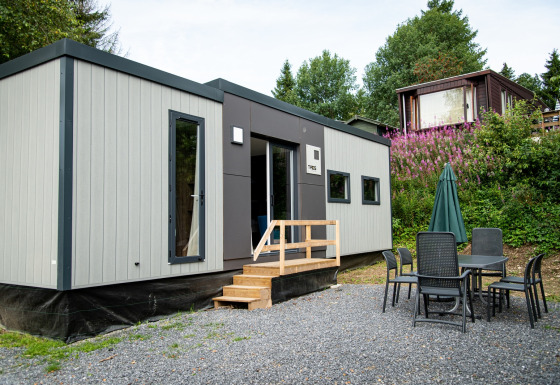 Un moderno lodge Taos XL en Petite Suisse, Bélgica, con mesa y sillas exteriores en un entorno natural.