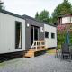 Et moderne Taos XL-lodge ved Petite Suisse i Belgien, omgivet af træer og havemøbler udendørs.