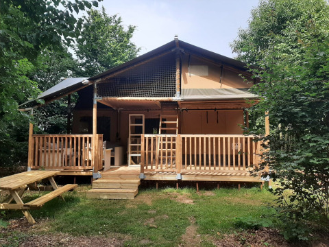 Safaritent Ranger Lodge met houten veranda, omringd door bomen en een picknickbank aan de voorkant.