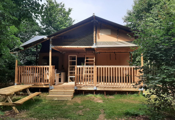 Tienda safari llamada Ranger Lodge con porche de madera, rodeada de árboles y banco de picnic adelante.