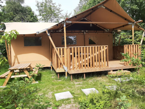 Tienda safari Dreamer en Petite Suisse, Bélgica, rodeada de vegetación y con terraza y mesa de picnic.