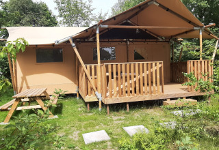 Tienda safari Dreamer en Petite Suisse, Bélgica, rodeada de vegetación y con terraza y mesa de picnic.