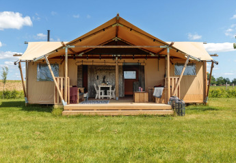 Tenda safari con veranda coperta su prato verde sotto cielo blu, arredata per un soggiorno confortevole.
