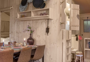 Interieur van Dreamer safaritent bij Petite Suisse, België, met houten meubels en een knusse eethoek.