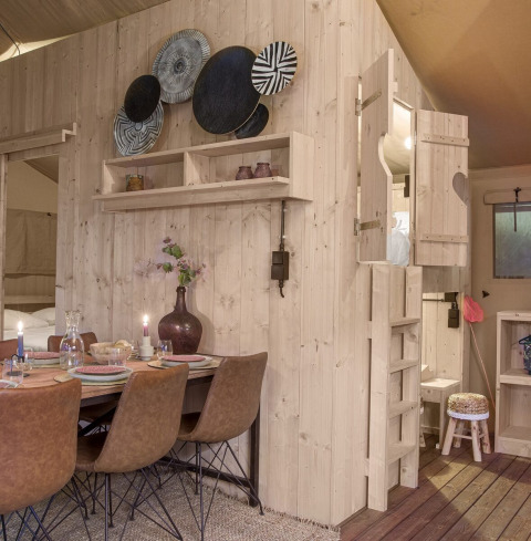Interno della tenda safari Dreamer a Petite Suisse, Belgio, con arredo in legno e zona pranzo accogliente.