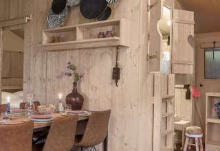 Interieur van Dreamer safaritent bij Petite Suisse, België, met houten meubels en een knusse eethoek.