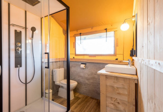 Baño dentro de la tienda safari Dreamer en Petite Suisse, Bélgica, con ducha moderna y decoración de madera.