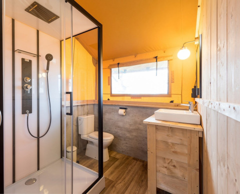 Baño dentro de la tienda safari Dreamer en Petite Suisse, Bélgica, con ducha moderna y decoración de madera.
