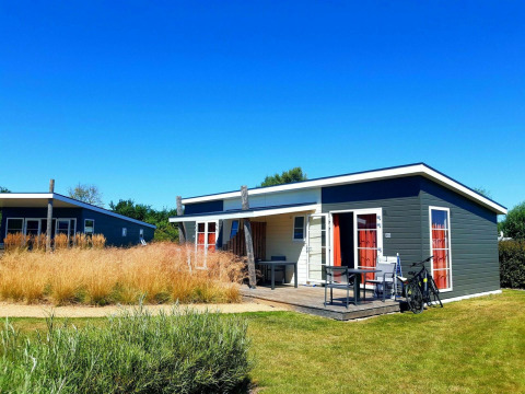 Pequeña casa moderna Comfort Lodge en Kompas Camping - Westende, Bélgica, bajo un cielo azul brillante.