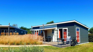 Pequeña casa moderna Comfort Lodge en Kompas Camping - Westende, Bélgica, bajo un cielo azul brillante.