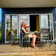En kvinde og et barn sidder foran et tiny house Comfort Lodge ved Kompas Camping Westende i Belgien.