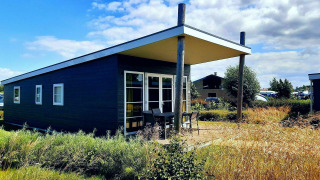 Comfort Lodge en Kompas Camping - Westende, Bélgica, rodeada de vegetación y cielo azul brillante.