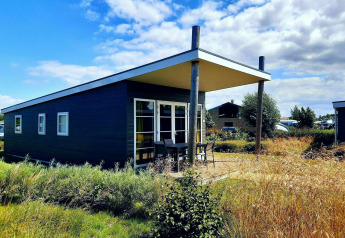 Comfort Lodge en Kompas Camping - Westende, Bélgica, rodeada de vegetación y cielo azul brillante.