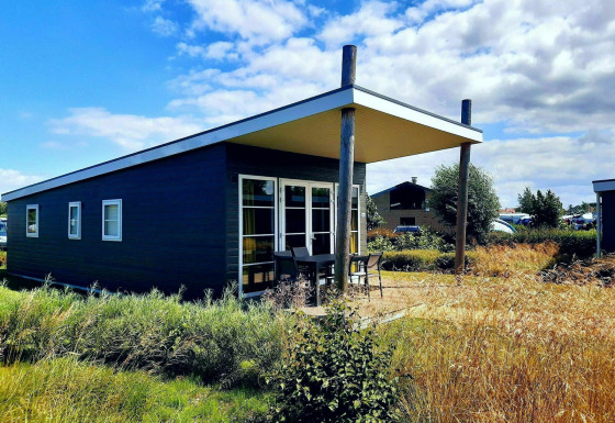 Comfort Lodge en Kompas Camping - Westende, Bélgica, rodeada de vegetación y cielo azul brillante.