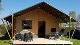 Safari tent at De Scherpenhof in the Netherlands with a wooden deck, chairs, and outdoor seating area.