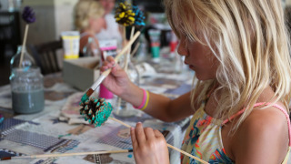 Een kind schildert een dennenappel tijdens een creatieve workshop op Vakantiepark Bonte Vlucht in Utrecht.